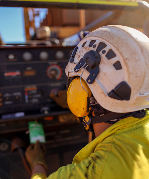A worker using heavy machinery wears a helmet and earmuffs