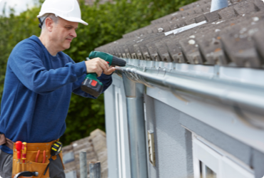 A contractor fixes a gutter while standing on a ladder