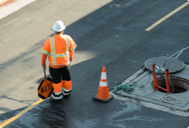 A worker control traffic next to an open manhole