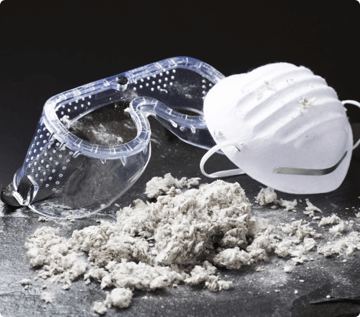 Safety goggles and a facemask sits next to a pile of asbestos