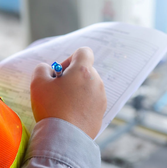 Safety Audit Services And Preparation Safety audit inspector checking off items on his paperwork wearing an orange vest